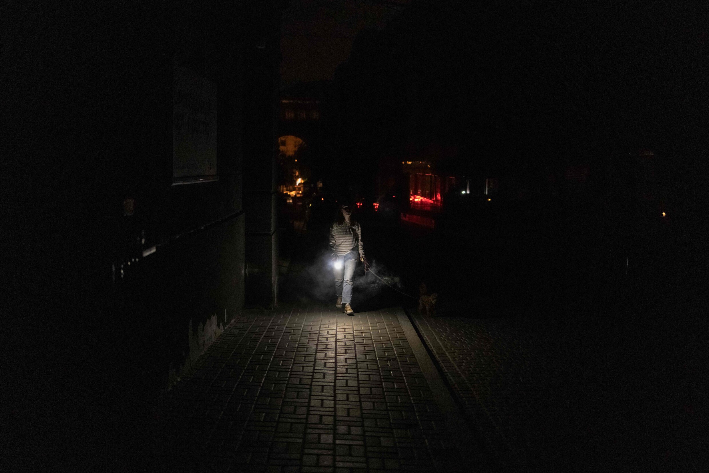 Een vrouw in Kyiv laat haar hond uit in het pikdonker, nadat door Russische aanvallen de Oekraïense stroomvoorziening deels wegviel.